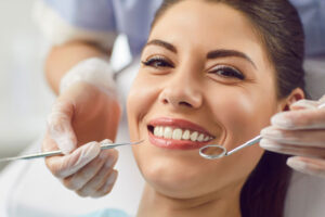Smiling woman during dental checkup with tools near her teeth.