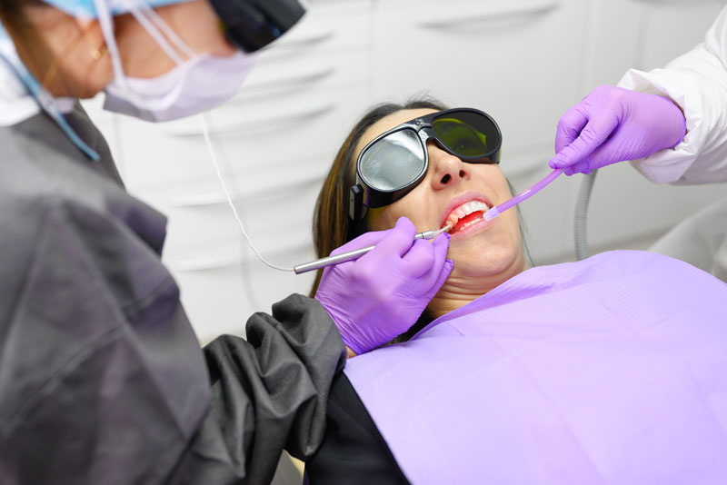 Dentist performing laser dental treatment on a patient wearing protective glasses in a dental clinic